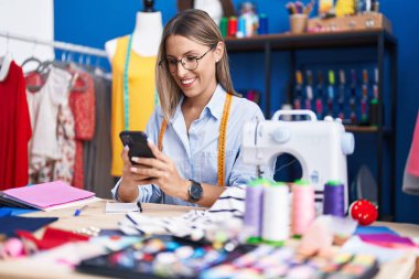 Elbise fabrikasında akıllı telefon kullanan, kendine güvenen, güzel İspanyol bir terzi.