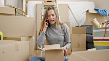 Karton kutuları açan beyaz bir kadın telefonda konuşuyor. Yeni evde şikayet ediyor.