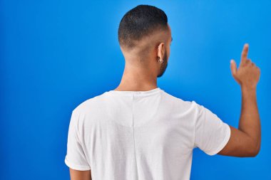 Genç İspanyol adam mavi arka planda dikiliyor. Geriye doğru poz veriyor. 