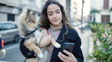Köpekli genç İspanyol kadın sokakta akıllı telefon kullanıyor.
