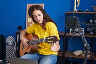 Young woman musician playing classical guitar at music studio