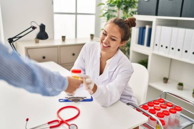 Genç, güzel İspanyol kadın doktor klinikte idrar testi tüpü tutuyor.