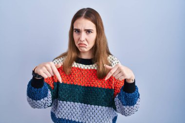 Mavi arka plan üzerinde duran genç İspanyol kız üzgün ve üzgün görünüyor, parmaklarıyla yön gösteriyor, mutsuz ve depresif.. 