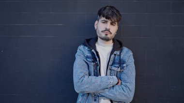 Ciddi bir ifadeyle duran ve izole edilmiş siyah arka planda kollarını kavuşturan İspanyol genç bir adam.