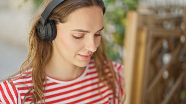 Kahve dükkanının terasında oturan ve kulaklık takan genç sarışın kadın.