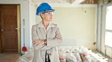 İnşaat alanında kollarını kavuşturmuş orta yaşlı sarışın bir mimar.