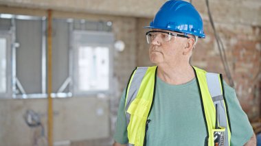 İnşaat alanında gevşek bir ifadeyle duran orta yaşlı gri saçlı adam müteahhit.