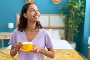 Young african american woman drinking cup of coffee sitting on bed at bedroom