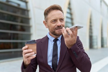 Orta yaşlı bir iş adamı akıllı telefondan konuşuyor sokakta kahve içiyor.