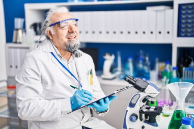 Middle age grey-haired man scientist writing report working at laboratory