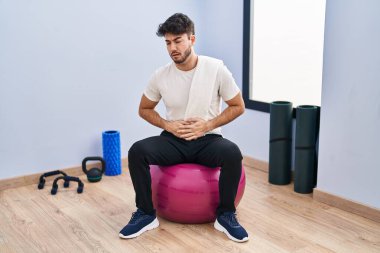 Sakallı İspanyol bir adam yoga odasında elleri ve karnında pilatese oturmuş çünkü hazımsızlık, acı verici bir hastalık kendini iyi hissetmiyor. Ağrı kavramı. 