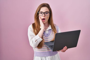 Bilgisayar laptopu kullanan beyaz bir kadın korkmuş ve şok olmuş, şaşırmış ve şaşırmış bir şekilde yüz ifadesi takınıyor. 