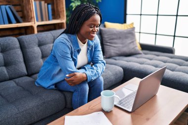 African american woman using laptop drinking coffee at home