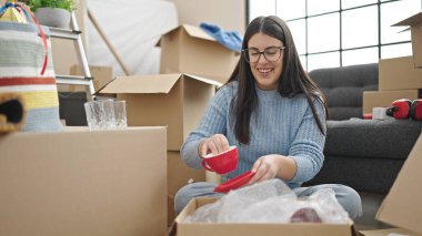 Young hispanic woman smiling confident unpacking cardboard box at new home