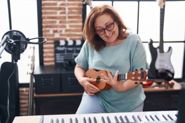 Müzik stüdyosunda ukulele çalarken gülümseyen son sınıf bayan müzisyen.