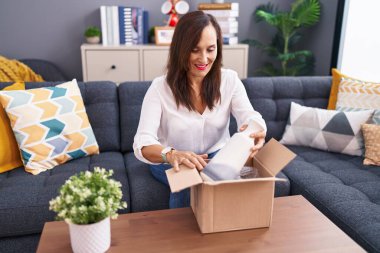 Genç ve güzel İspanyol kadın evdeki masada oturan karton kutu kutusunu boşaltıyor.