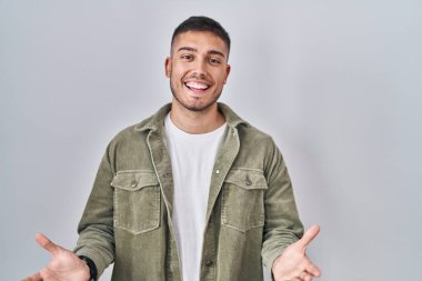 Young hispanic man standing over isolated background smiling cheerful with open arms as friendly welcome, positive and confident greetings 