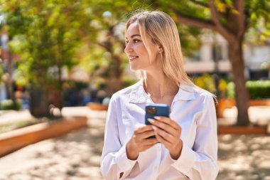 Parkta akıllı telefon kullanan, kendine güvenen genç sarışın kadın.