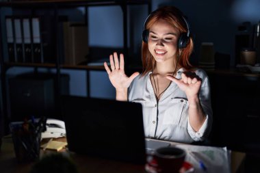 Geceleri ofiste çalışan beyaz bir kadın altı numaralı parmaklarını gösterip işaret ederken kendinden emin ve mutlu bir şekilde gülümsüyor.. 