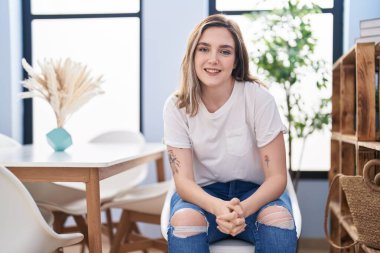 Young woman smiling confident sitting on chair at home