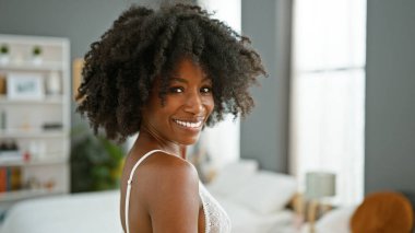 Afro-Amerikalı kadın gülümsüyor. Yatak odasında seksi görünüyor.