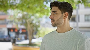 Genç İspanyol bir adam parkta ciddi bir ifadeyle yan tarafa bakıyor.