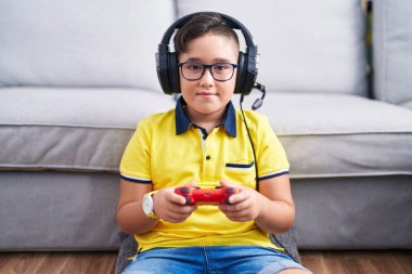 Yüzünde mutlu ve havalı bir gülümseme olan kulaklık takan İspanyol asıllı bir çocuk video oyunu oynuyor. şanslı kişi. 