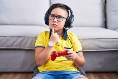 Kulaklık takıp video oyunu oynayan, kulaklık takan, parmakları çenesinde şüpheye odaklanmış genç İspanyol çocuk. 