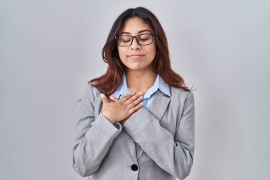 İspanyol genç iş kadını gözlük takıyor elleri göğsünde, gözleri kapalı gülümsüyor ve yüzünde minnet ifadesi var. sağlık kavramı. 