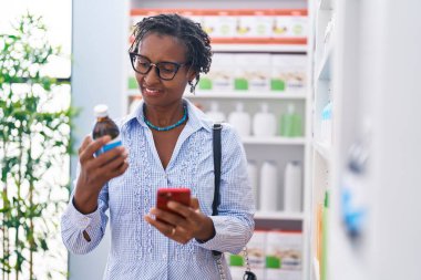 Orta yaşlı Afro-Amerikan kadın müşteri eczanede akıllı telefon ilaç şişesi kullanıyor.