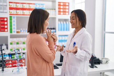 Eczanede konuşan iki kadın eczacı ve müşteri.