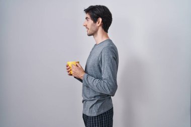 Genç İspanyol adam pijama giyip bir fincan kahve içiyor. Yan tarafa bakıyor, profil pozu veriyor. Doğal bir yüzü ve kendine güvenen bir gülümsemesi var.. 