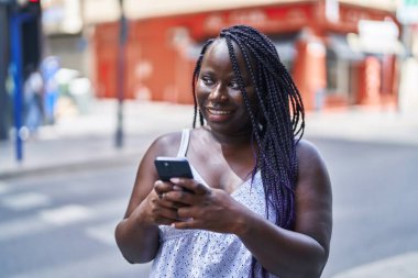 Afro-Amerikalı kadın sokakta akıllı telefon kullanarak kendine güveniyor.