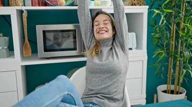 Beyaz bir kadın yemek salonunda masada oturmuş kollarını açıyor.