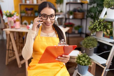 Çiçekçide akıllı telefondan konuşan genç Arap kadın çiçekçi.