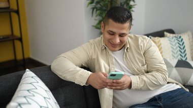 Evdeki kanepede oturan, akıllı telefon kullanan genç bir İspanyol.