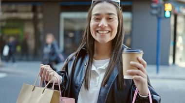 Genç ve güzel İspanyol kadın gülümsüyor. Elinde alışveriş poşetleri ve kahvelerle caddede.