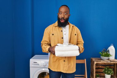 Afrika kökenli Amerikalı adam çamaşır odasında temiz havlu tutuyor. Şaşırmış ve şaşırmış bir ifadeyle korku ve heyecanlı bir yüz ifadesi var.. 