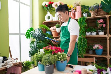 Young chinese man florist using touchpad touching plant at flower shop