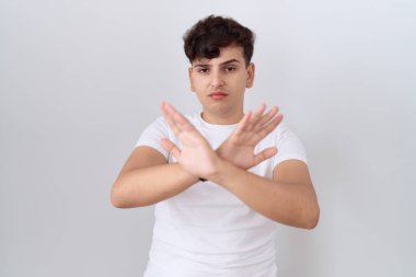 Gündelik beyaz tişört giyen genç bir adam. Reddedilmiş yüz ifadesi. Kollar çapraz, avuç içleri negatif, kızgın yüz ifadesi. 
