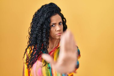 Sarı arka planda dikilen orta yaşlı İspanyol kadın avucuyla şarkı söylemeyi kesiyor. Yüzünde olumsuz ve ciddi bir jest olan uyarı ifadesi. 