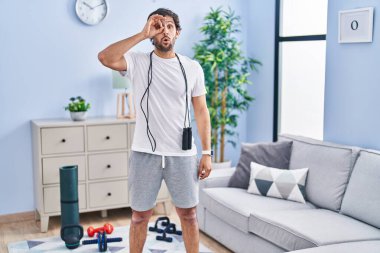 Evde spor giyinen yakışıklı Latin adam şaşırmış yüz ifadesiyle şaşırmış, parmaklarının arasından bakıyor. İnançsız ifade. 