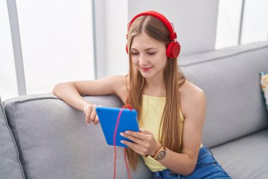 Young caucasian woman watching video on touchpad sitting on sofa at home