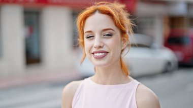 Caddede kendine güvenen genç kızıl saçlı kadın gülümsüyor