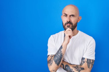 Mavi arka planda duran İspanyol dövmeli adam bir soru hakkında endişeli ve gergin düşünüyor. 