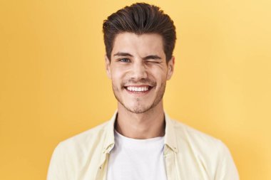 Sarı arka planda duran genç İspanyol adam kameraya seksi bir ifadeyle bakıyor, neşeli ve mutlu bir yüzle.. 