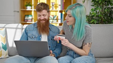 Kadın ve erkek kanepede dizüstü bilgisayar ve kredi kartıyla alışveriş yapıyorlar.