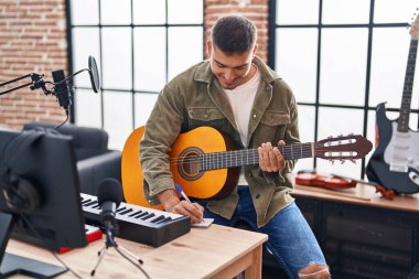 Young hispanic man musician composing song playing classical guitar at music studio