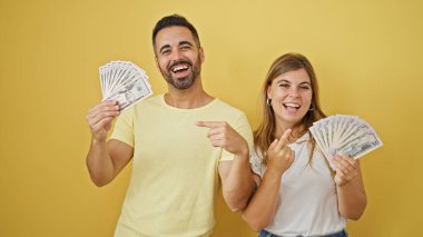 Erkek ve kadın çift gülerek izole edilmiş sarı arka planda dolarlara işaret ediyorlar.