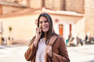 Genç, güzel, İspanyol bir kadın gülümsüyor ve caddede akıllı telefondan konuşuyor.